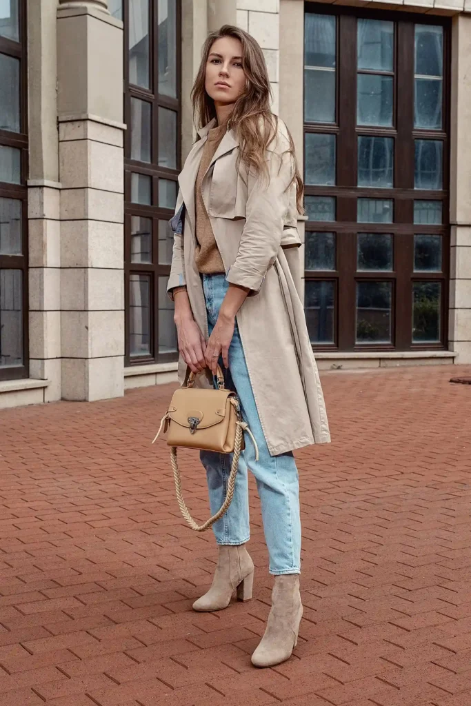 Woman wearing a beige trench coat, light-blue jeans and ankle boots