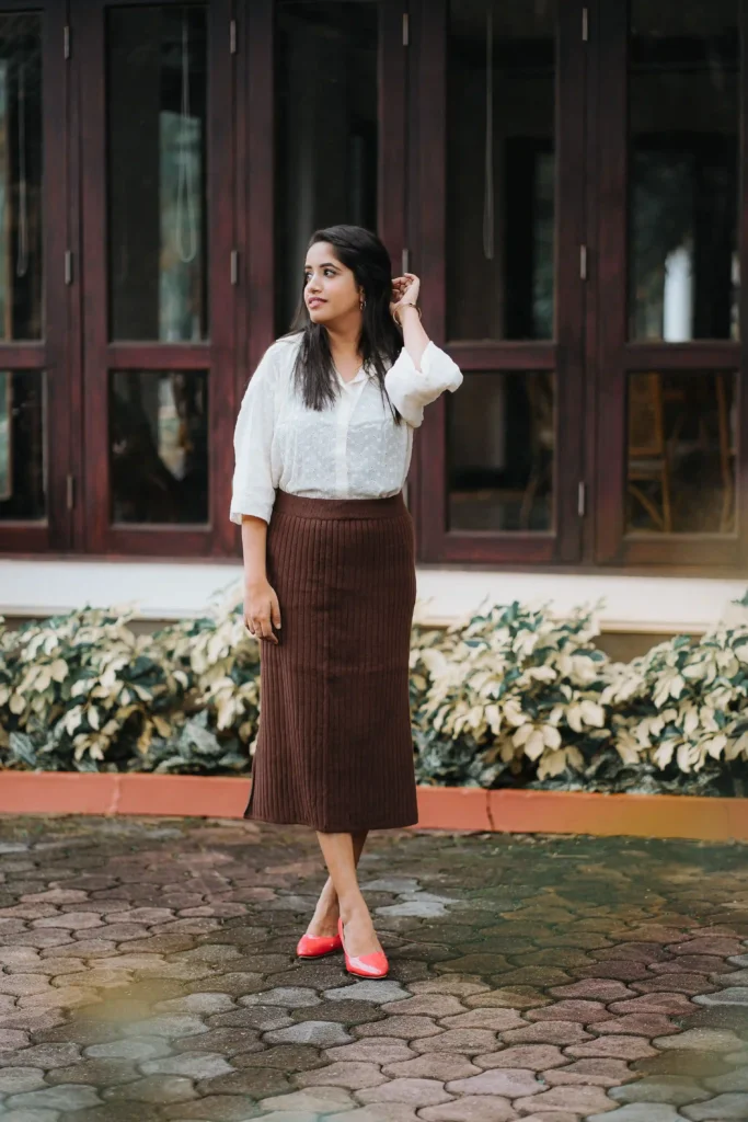 Woman wearing a white blouse, brown ribbed midi skirt and coral-pink flats outdoors.