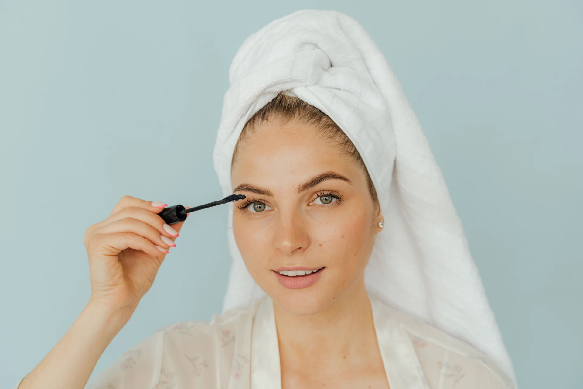 Woman wearing a white head towel applying mascara to her eyelashes