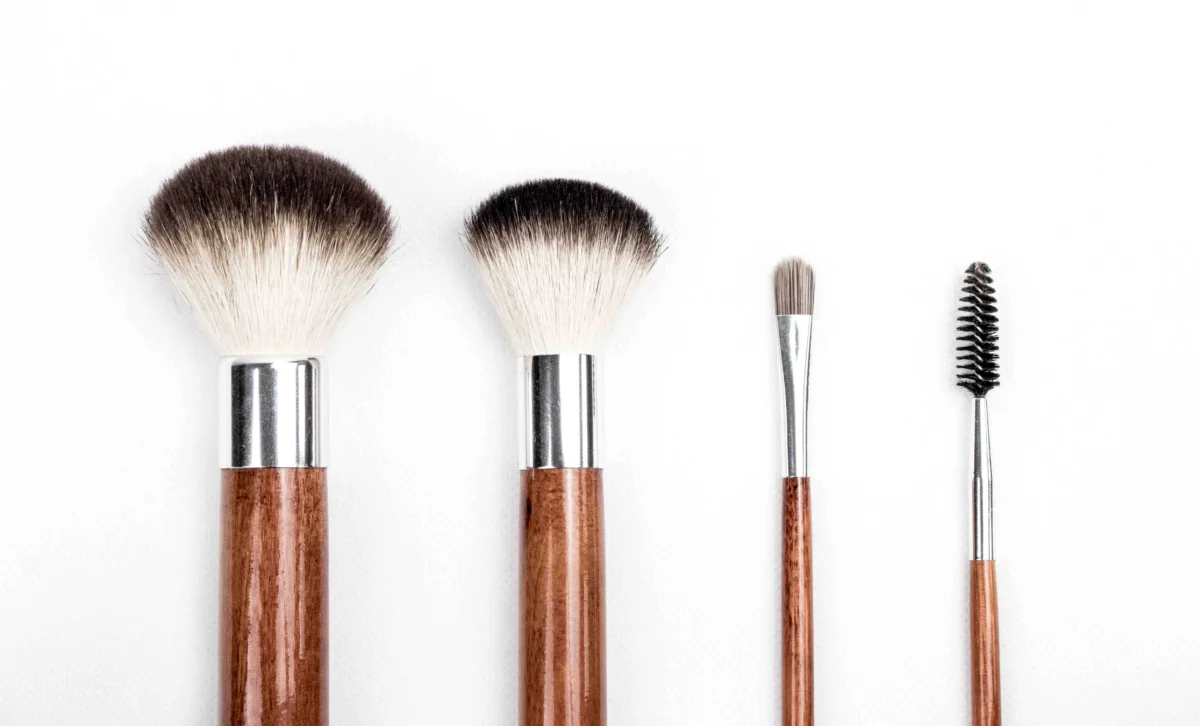 Four makeup brushes with wooden handles and silver ferrules arranged on a white background.