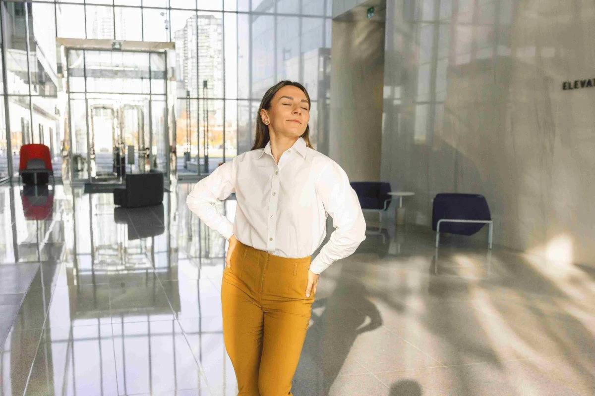 Woman wearing a white button-down shirt and mustard trousers in a modern office lobby