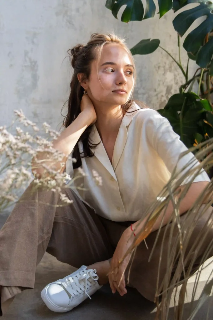 Woman wearing a loose white shirt, brown wide-leg trousers and white sneakers