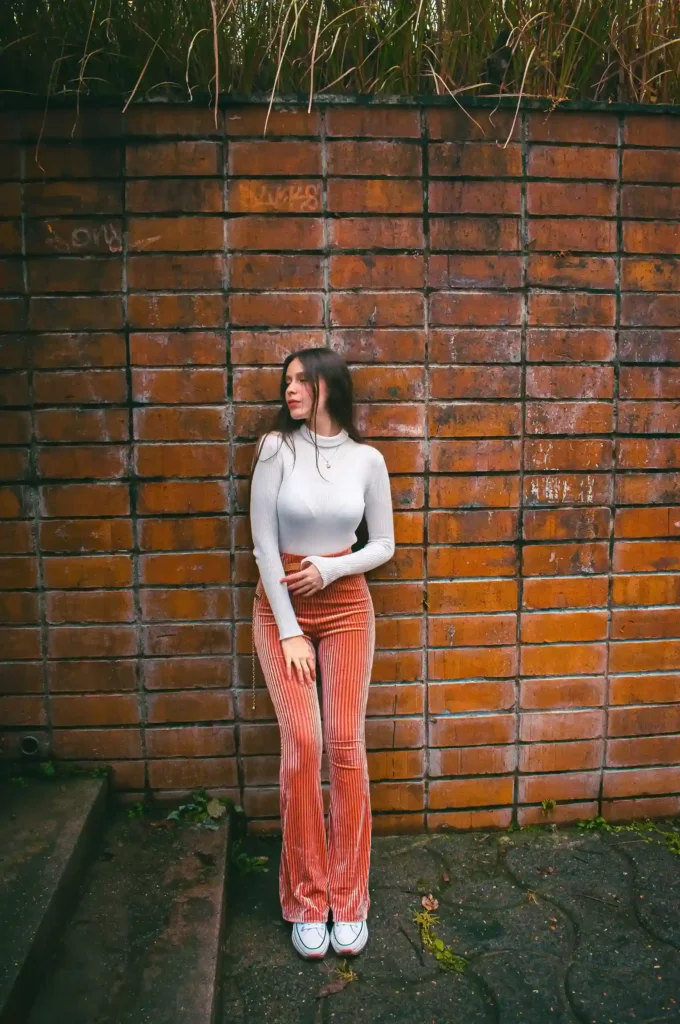 Woman wearing a fitted white top, rust-colored flared trousers and white sneakers
