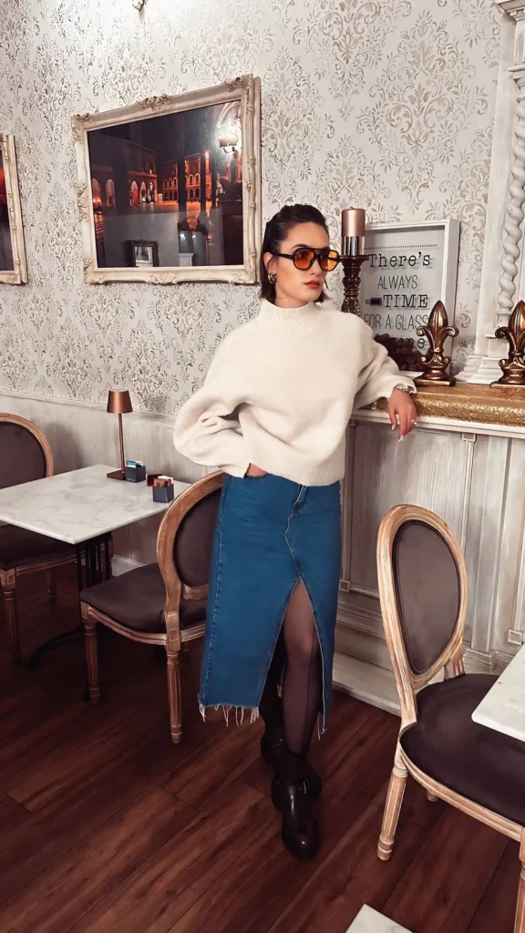 Woman wearing a chunky white turtleneck, denim midi skirt, tights and black boots