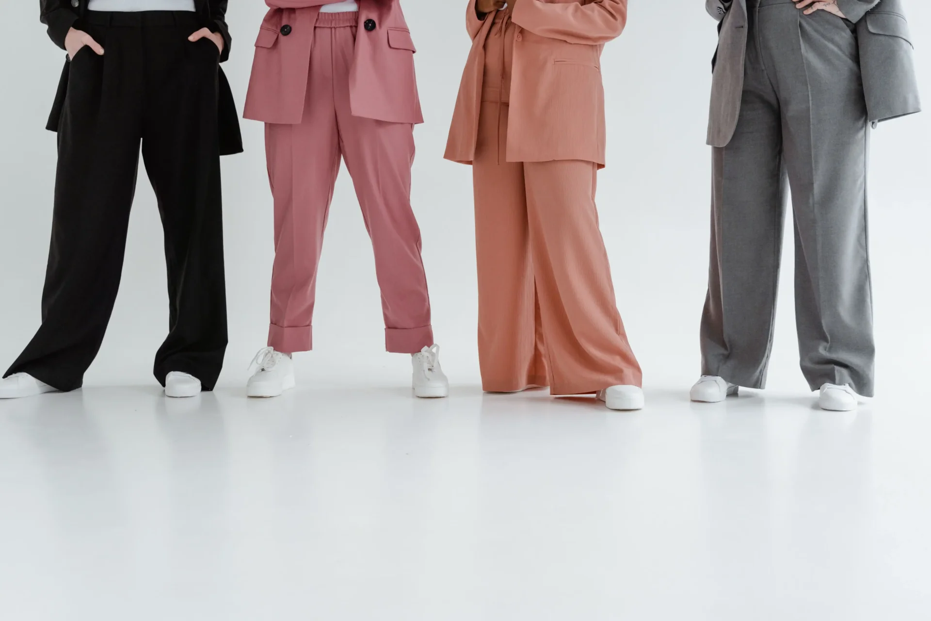 Four people wearing black, pink, peach and gray wide-leg trousers with white sneakers